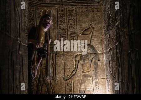 Une touriste féminine regarde autour du coin dans un passage faiblement éclairé dans un ancien temple égyptien. Banque D'Images