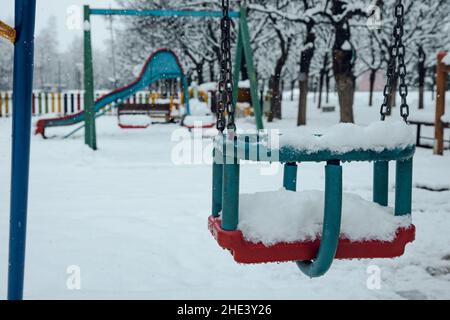 Aire de jeux avec balançoire en métal pour enfants.Glissez dans l'arrière-plan.L'aire de jeux vide est couverte de neige.Saison d'hiver dans les Balkans. Banque D'Images