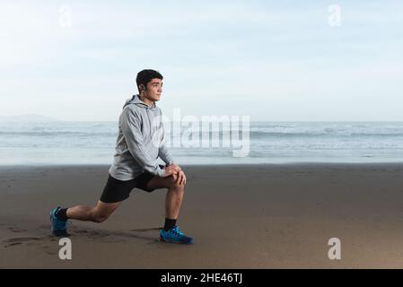 Adolescent hispanique s'étirant à la plage tandis que est concentré sur ses buts Banque D'Images