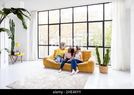 Photo intérieure de trois jeunes femmes heureuses assises sur un canapé Banque D'Images