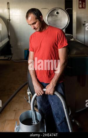 Agriculteur remplissant un récipient de lait frais de la ferme laitière. Banque D'Images