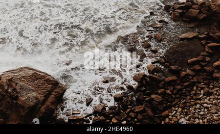 Une vue de dessus des vagues mousseuse qui éclabousse sur les rochers de la côte Banque D'Images