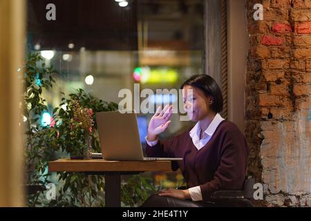 Jeune femme afro-américaine amicale travaillant à distance dans un café, donnant une leçon en ligne par ordinateur portable Banque D'Images