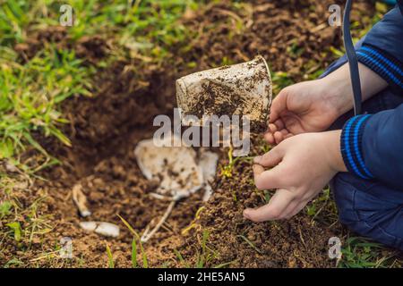 Le garçon joue recyclage. Il enterrer des plats jetables en plastique et des plats biodégradables. Après quelques mois, il a creusé les plats et a vu que le Banque D'Images