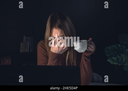 Jeune femme fatiguée travaillant derrière un ordinateur portable la nuit, les yeux malades. Banque D'Images