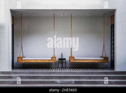 Chiang Rai,Thaïlande - 06 sept, 2020 : coin détente avec chaises balançoires en bois avec coussins de suspension sur la chaîne d'or et table latérale avec mur blanc Banque D'Images