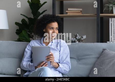 Jeune femme africaine rêveuse tenant une tablette numérique. Banque D'Images