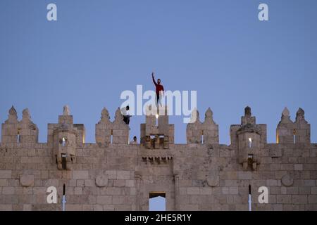 Le jeune palestinien marque le signe de la victoire alors qu'il se tient au-dessus du mur ottoman crénelé au-dessus de la porte de Damas, à l'extrémité nord de la vieille ville de Jérusalem-est d'Israël Banque D'Images