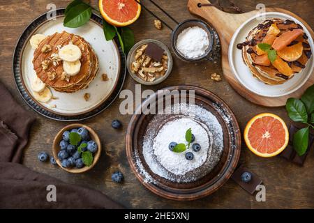 Fête du Pancake, petit déjeuner sain.Délicieux crêpes américaines faites maison à la banane avec des bleuets, des noix, du caramel, du chocolat, de l'orange rouge sur le rus Banque D'Images