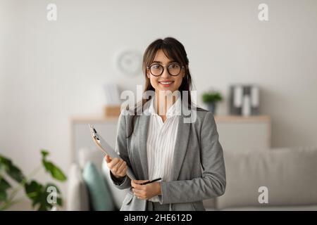 Portrait d'une femme gaie psychologue posant avec un presse-papiers, regardant et souriant à la caméra, travaillant dans un bureau moderne Banque D'Images