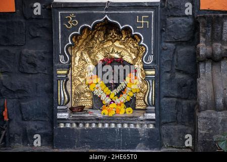 Photo de stock de beau petit temple de lord ganesha gravé sur le mur peint de couleur noire. Lampe à huile en argile faite près de l'idole, offrant une guirlande Banque D'Images