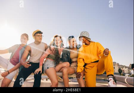 Les amis rient les uns avec les autres tout en étant assis ensemble au soleil.Des jeunes heureux qui se réjouissant de passer un bon moment en ville.Groupe d'amis Banque D'Images