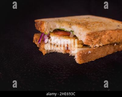 sandwich grillé à moitié mangé avec tomate, oignon, poulet, laitue et pain multi-grain. gros plan avec espace de copie et fond sombre. Banque D'Images