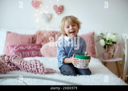 Mignon enfant blond avec chemise, assis sur le lit avec décoration de Saint-Valentin, arrière-plan isolé Banque D'Images