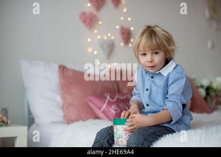 Mignon enfant blond avec chemise, assis sur le lit avec décoration de Saint-Valentin, arrière-plan isolé Banque D'Images