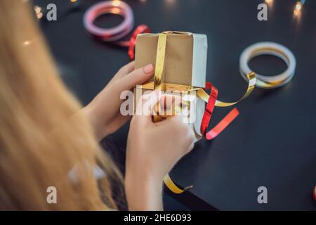 Jeune femme est présente d'emballage. Présent enveloppé dans du papier craft avec un ruban rouge et or pour Noël, anniversaire, fête des mères ou la saint valentin Banque D'Images