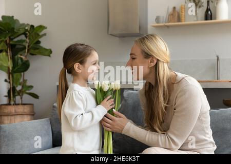 Adorable petite fille donnant un bouquet de fleurs à une maman heureuse Banque D'Images