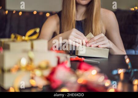 Jeune femme est présente d'emballage. Présent enveloppé dans du papier craft avec un ruban rouge et or pour Noël, anniversaire, fête des mères ou la saint valentin Banque D'Images