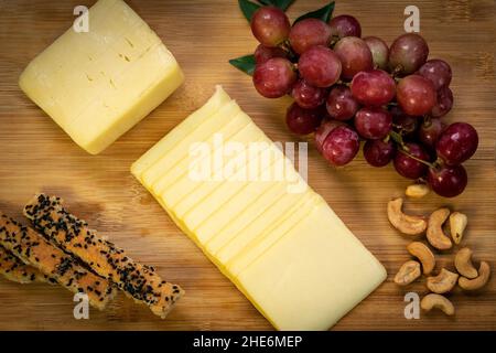 Tranche de fromage cheddar tranché sur une planche à bois avec des raisins, des noix de cajou, des bâtonnets de pain et du miel Banque D'Images