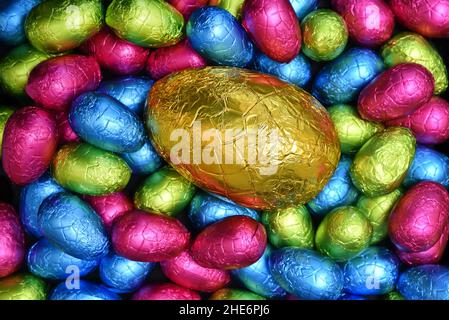 Pile ou groupe de plusieurs couleurs et différentes tailles d'oeufs de pâques au chocolat enveloppés d'une feuille colorée en rose, bleu, jaune et vert lime. Banque D'Images