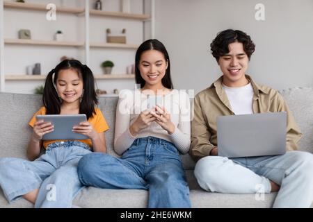 Jeune enfant et jeune asiatique souriant mère et père surfant sur Internet, bavardant sur des gadgets, jouer au jeu Banque D'Images