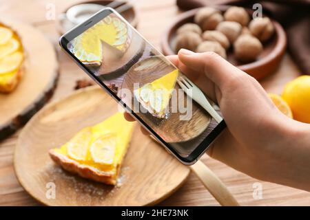 Femme avec téléphone mobile prenant la photo de tarte au citron savoureuse sur la table Banque D'Images