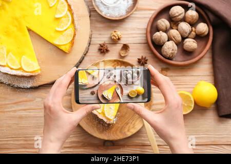 Femme avec téléphone mobile prenant la photo de tarte au citron savoureuse sur la table Banque D'Images
