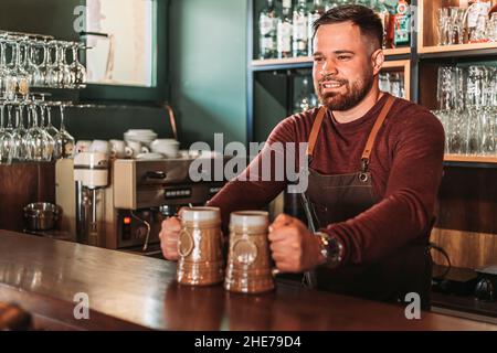 Un jeune barman barbu sert deux tasses de bières sur le comptoir Banque D'Images