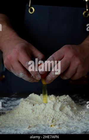 L'homme met le jaune d'œuf dans la farine.préparation de la pâte pour les boulettes.Pour faire de la pâte Banque D'Images