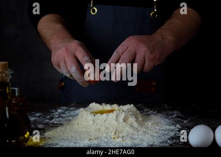 L'homme met le jaune d'œuf dans la farine.préparation de la pâte pour les boulettes.Pour faire de la pâte Banque D'Images