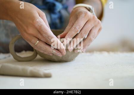 Gros plan des mains de maître de céramique femelle créant une tasse d'artisanat de pot humide.Table en atelier de poterie Banque D'Images