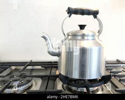 Et une bouilloire argentée à l'ancienne pour le thé avec bec verseur et pour manipuler l'eau bouillante sur une cuisinière à gaz avec espace café Banque D'Images
