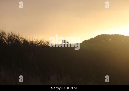 Beach Park, Dunure, Ayrshire, Écosse.Un banc unique silhoueté sur le sommet d'une colline herbeuse alors que le soleil d'hiver se couche Banque D'Images
