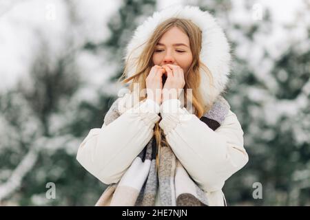 Bonne fille se réchauffant les mains dans des vêtements chauds d'hiver.Un portrait attrayant en plein air par temps froid.Congélation d'une femme à l'extérieur Banque D'Images