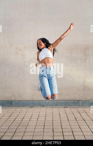 une jeune femme africaine saute heureuse et souriante avec un mur de béton gris en arrière-plan, le concept de jeunesse et de diversité raciale, l'espace de copie pour le texte Banque D'Images
