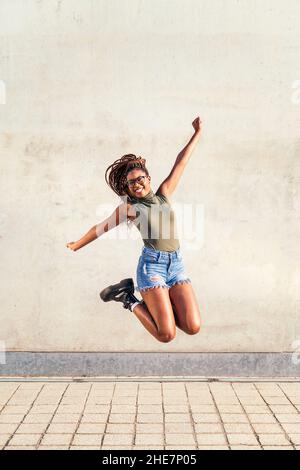 jeune femme noire saute heureux et souriant avec un mur en béton gris en arrière-plan, concept de jeunesse et de diversité raciale, espace de copie pour le texte Banque D'Images