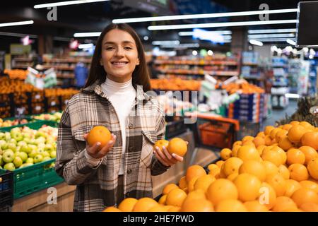 Portrait d'une femme souriante qui tient des oranges dans la section des fruits et légumes du supermarché Banque D'Images