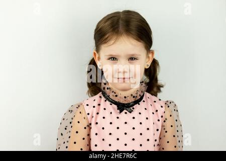 Petite fille souriante avec deux queues de cheval en robe à pois sur fond blanc Banque D'Images