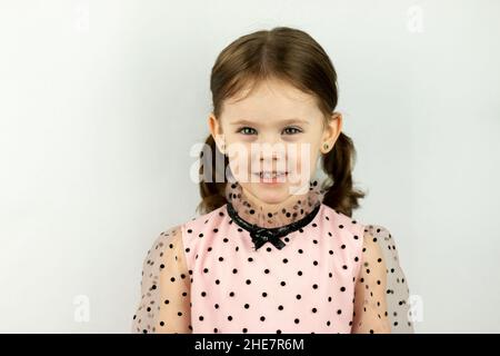 Petite fille souriante avec deux queues de cheval dans une robe avec des pois sur un fond blanc.Photo de studio Banque D'Images