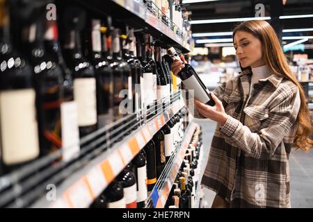 Une femme caucasienne choisit une bouteille de vin dans une épicerie.Acheter de l'alcool au supermarché Banque D'Images