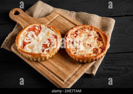 Deux délicieuses pizzas sur une planche à découper sur fond de bois noir.Style rustique. Banque D'Images