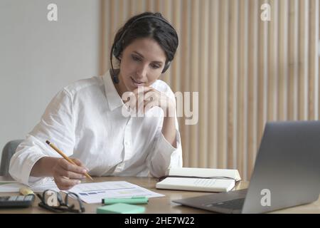 Jeune femme professionnelle consultante en affaires dans le micro-casque parler avec le client en ligne au bureau Banque D'Images