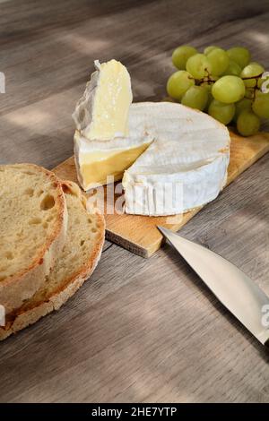 Camembert français de Normandie servi sur une planche à découper en bois avec des raisins et des tranches de pain. Banque D'Images