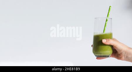 La main d'une femme tient un verre avec des smoothies verts sur un fond blanc.Bannière. Banque D'Images
