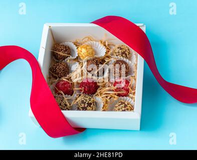 Chocolats faits à la main avec différentes garnitures dans une boîte blanche et un ruban rouge.Vue de dessus sur fond bleu.Photo de haute qualité Banque D'Images