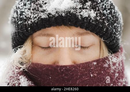 Gros plan sur le portait d'une femme blonde en bonnet beanie et nez recouverts de supports de foulard avec les yeux fermés en hiver.Portrait de saison d'hiver nordique Banque D'Images