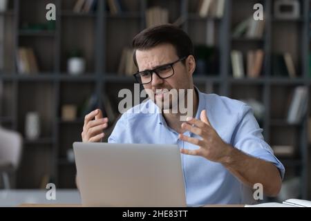 Un homme d'affaires mécontent dans des lunettes qui ont l'air d'utiliser un ordinateur portable Banque D'Images