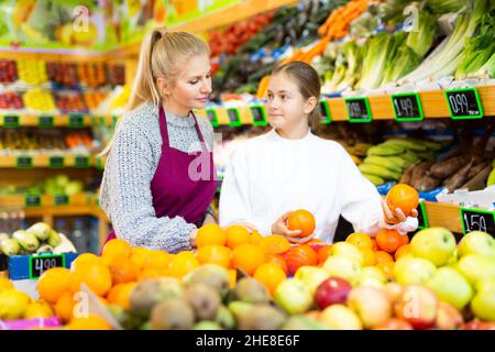 Une employée d'épicerie aide une adolescente à cueillir des fruits Banque D'Images