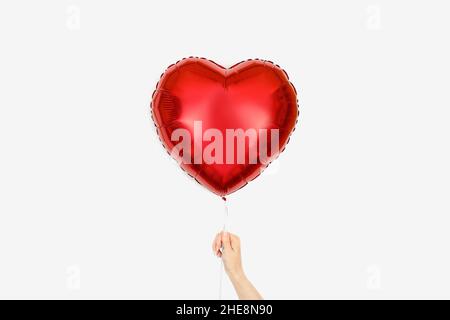 Ballon rouge de papier d'aluminium en forme de coeur sur fond blanc dans la main de la fille.Décoration de Saint-Valentin ou de mariage. Banque D'Images