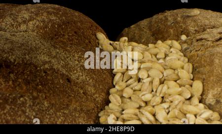 Pain frais délicieux isolé sur fond noir.Gros plan de pain rustique de seigle avec croûte croustillante et graines en chute, concept de nutri sain Banque D'Images